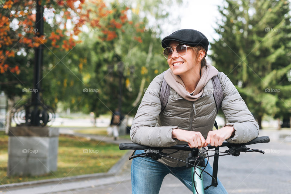 Young woman in cap on bicycle at autumn park in city