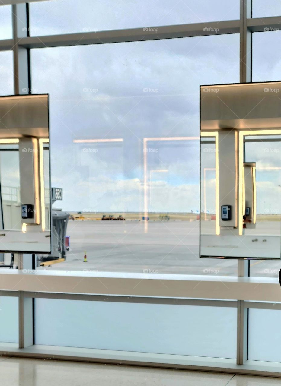 A window overlooking an airport taxiway is interrupted by mirrors reflecting other mirrors