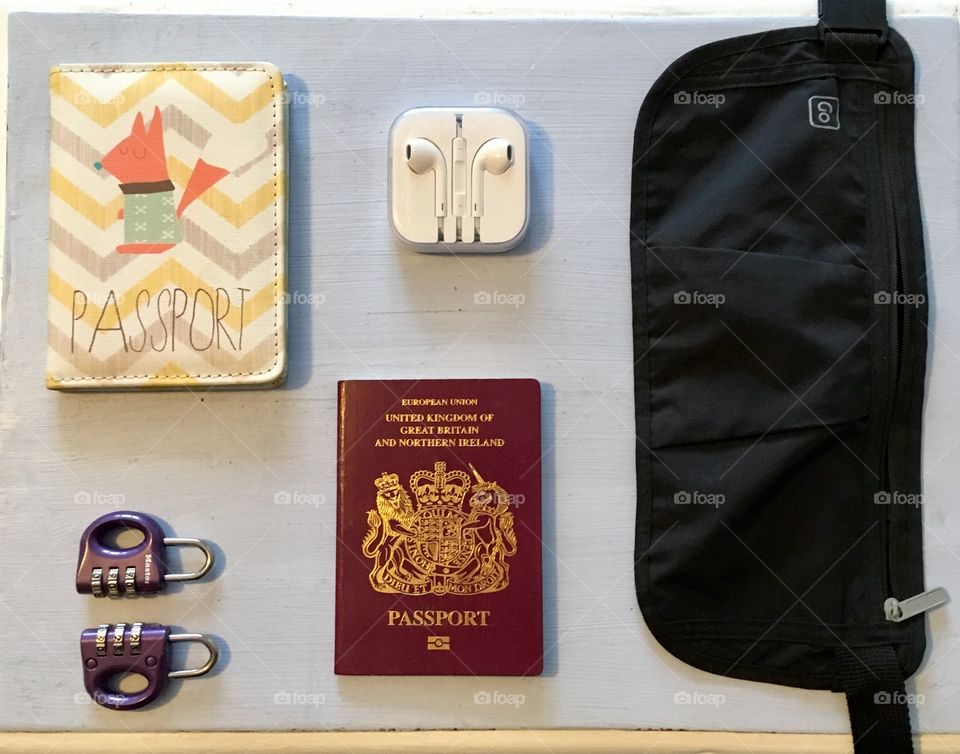 A top view of passports, padlocks, security pouch and headphones on a light blue background. Items ready for travel 