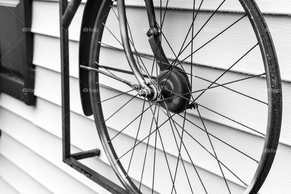 Closeup of a repurposed bicycle wheel hanging on the siding of a building 