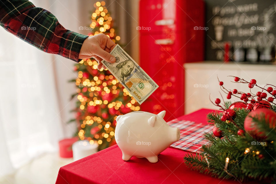 piggy bank with 100 dollars banknote in festive New Year atmosphere of scenery.  Magical bokeh with Christmas tree and bright lights.