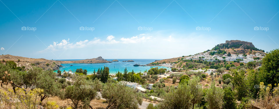 Panoramic view at Lindos town beneath clifftop ruins of ancient Acropolis and medieval castle.  Island of Rhodes. Greece.