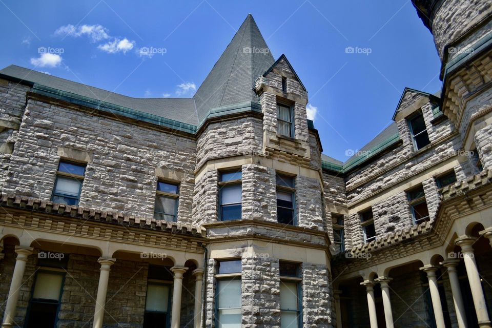 A grey brick building that looks like a castle with a pointed roof on top of a turret against a bright blue sky