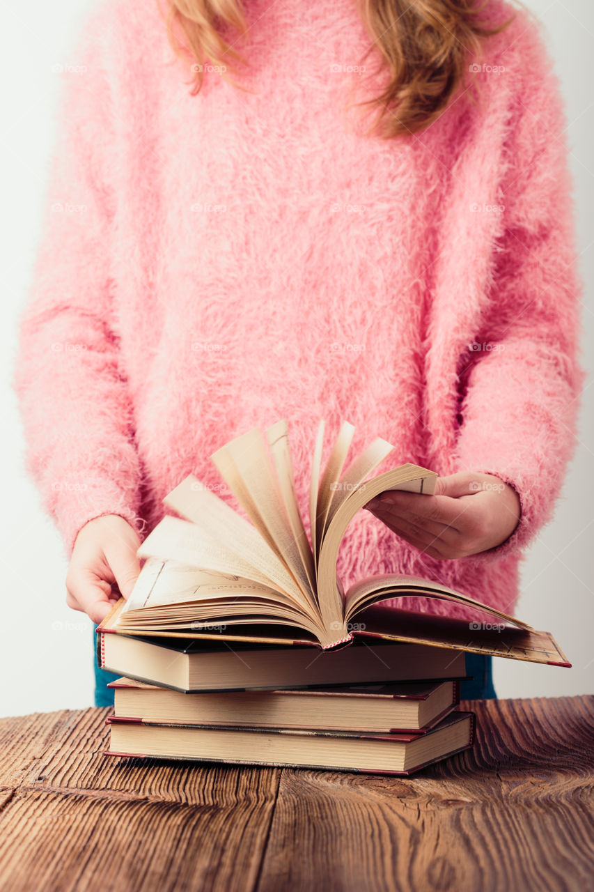 Young girl holding a few books. Teenager girl wearing pink sweater and blue jeans. Vertical photo
