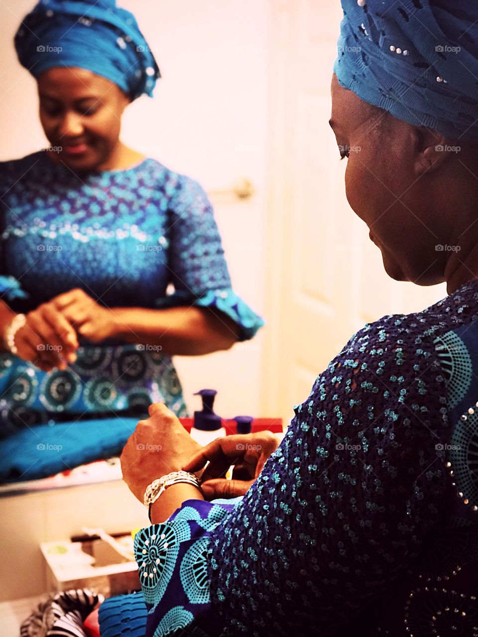 A woman in Nigerian attire taking off her jewelry after coming home on a Sunday morning.