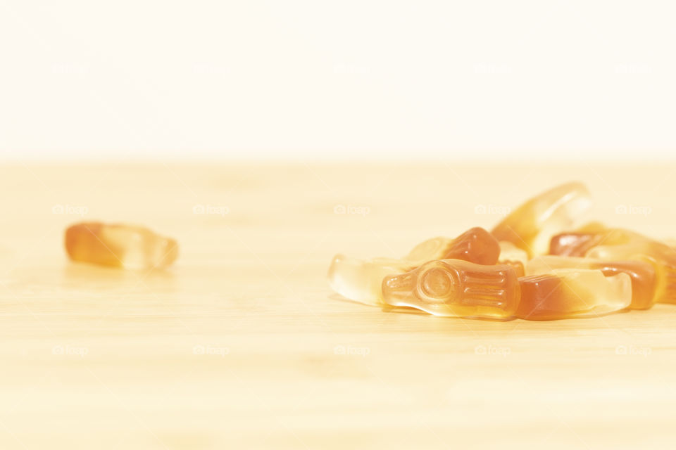 A portrait of multiple pieces of candy shaped as bottles of cola on a wooden table.