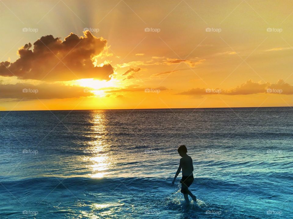 Young boy playing in the ocean in the light of a glorious beach sunset.