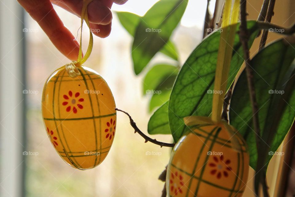 Closeup of a hand hanging a yellow easter egg on a plant