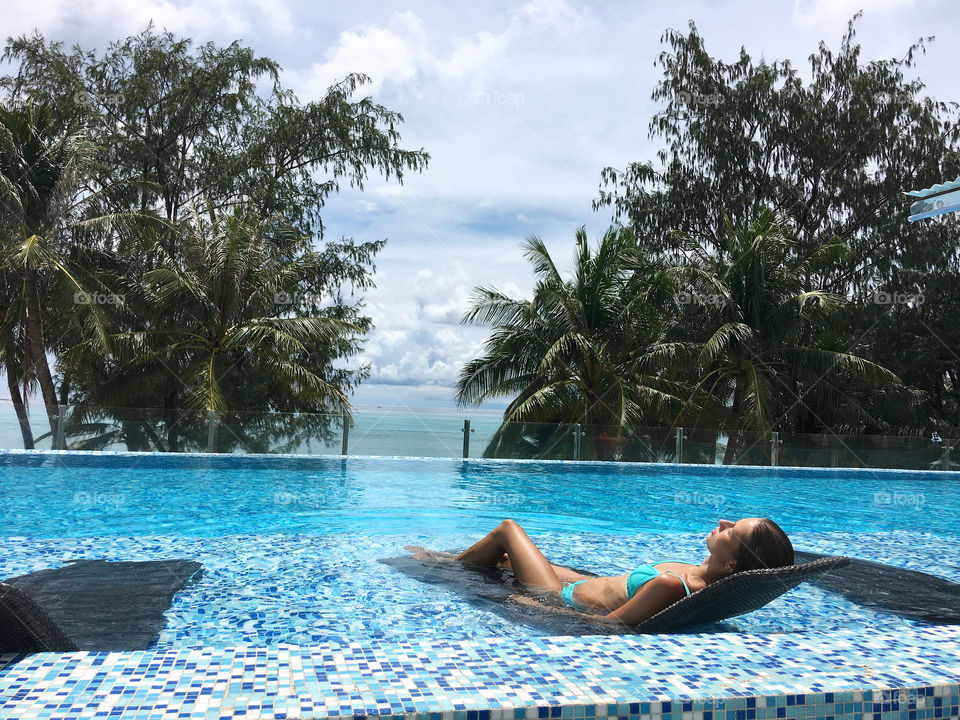 Young woman in bikini sunbathing on the swimming pool lounge 