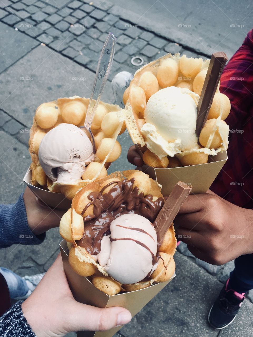 Three girls hold bubble waffle cones filled with icecream and chocolatey toppings 