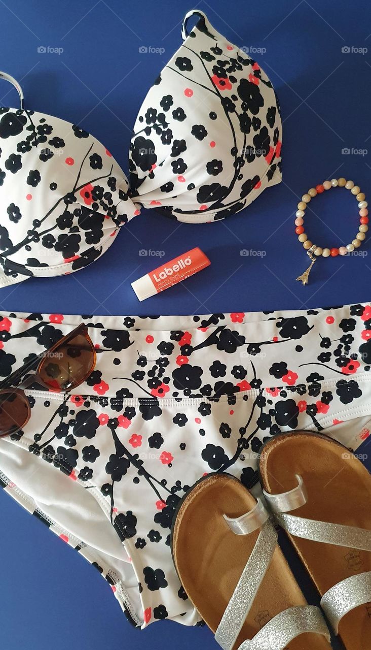 Labello peach shine product flatlay on a blue surfaced composed of a swimsuit, bracelet, sunglasses and flip flops