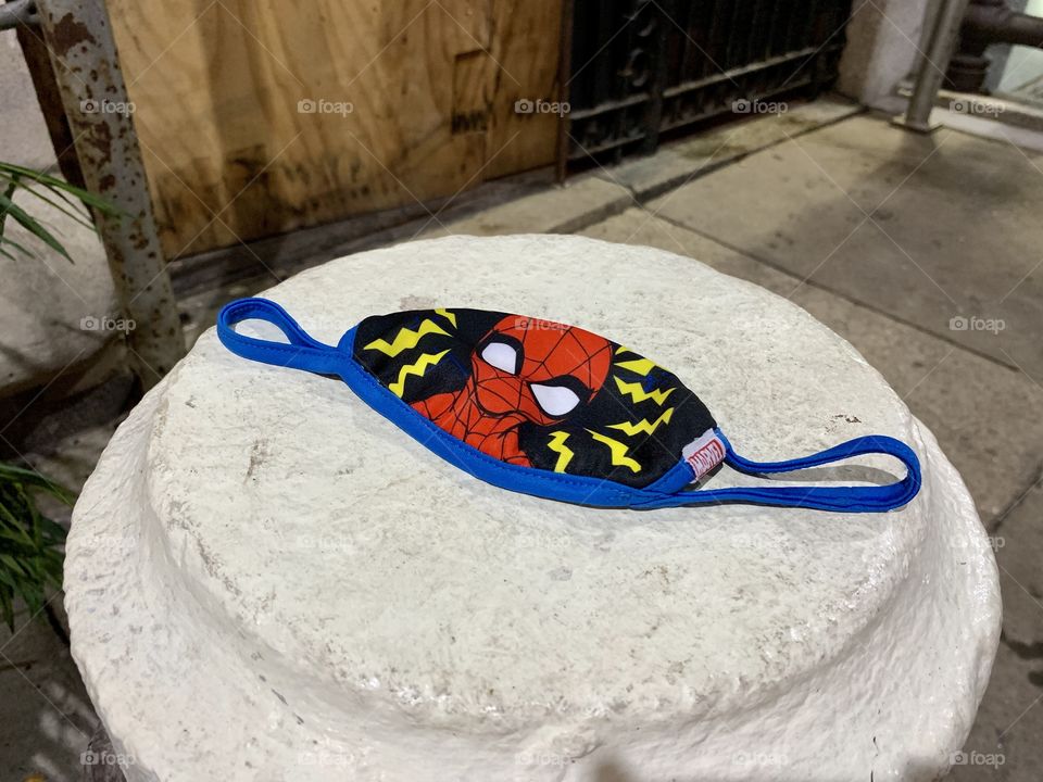 Spiderman mask for kids lying on a white cement under the scaffolding Street photography.