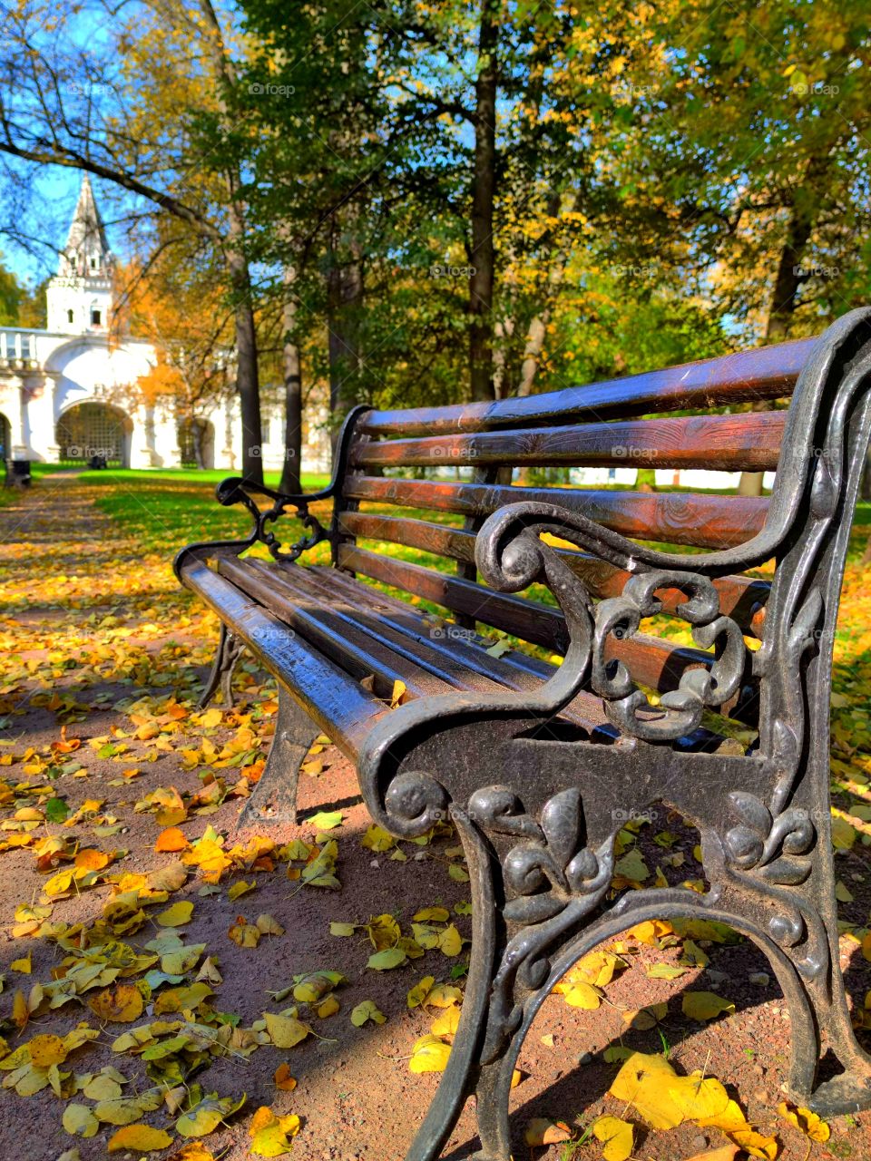 Autumn. Park.  Sunny day. Leaf fall. Wooden bench.  In the background a white fortress wall with a tower