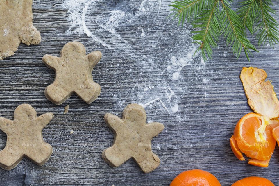 Christmas, gingerbread cookies on a wooden table sprinkled with flour, with tangerines and a green Christmas tree.