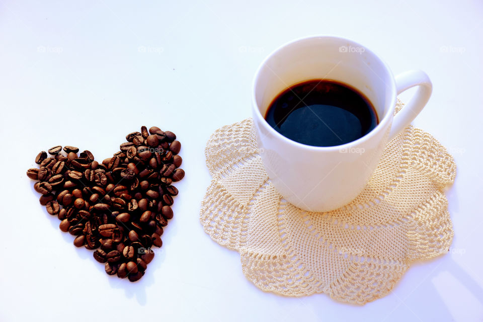 Heartshape made from coffee beans near coffee cup