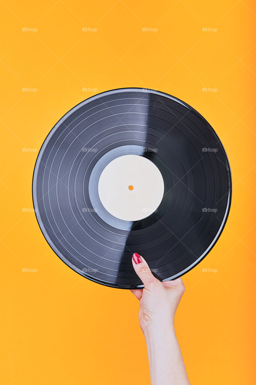 Female hand holding black vinyl record over a plain orange background. Minimal style