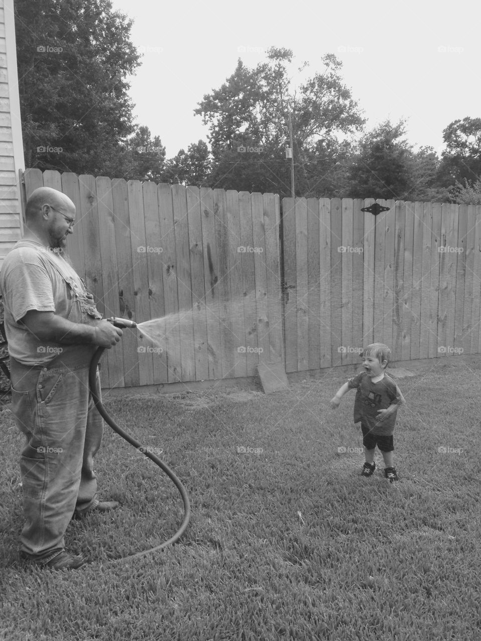 Grandpa spraying grandchild with water from water hose