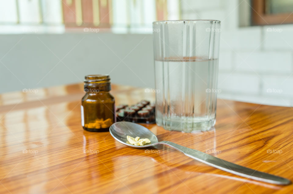View of antioxidants vitamin tablet, pill blisters, a bottle of drug, capsule in measuring spoon, with glass of water placed on the table. Medical Pharmacy theme. Side view, Close up with copy space.