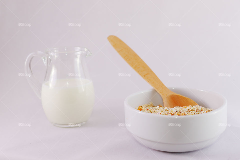 Oatmeal with yellow apricot pieces in a deep white bowl, a wooden spoon, a jar of milk. Ingredients for cooking oatmeal.