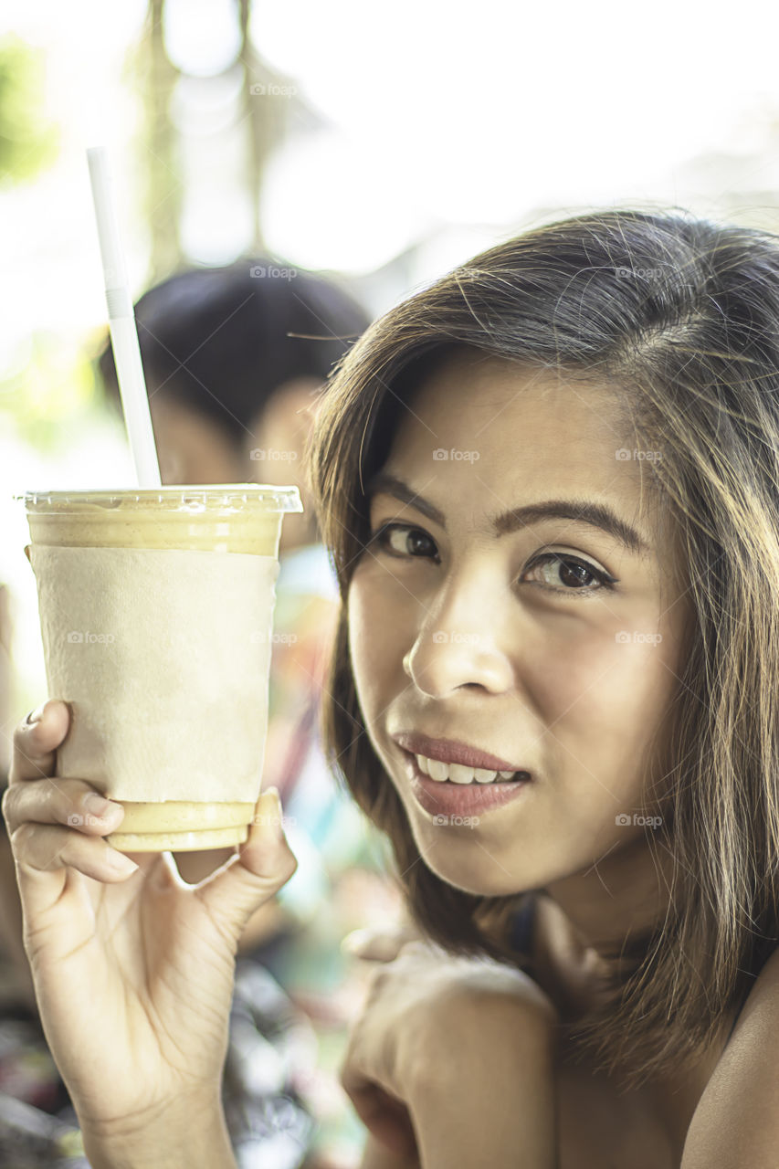 Asian woman holding glass of iced coffee.