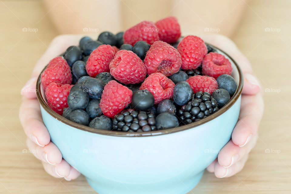 Delicious summer berries in a bowl in hands, healthy eating concept