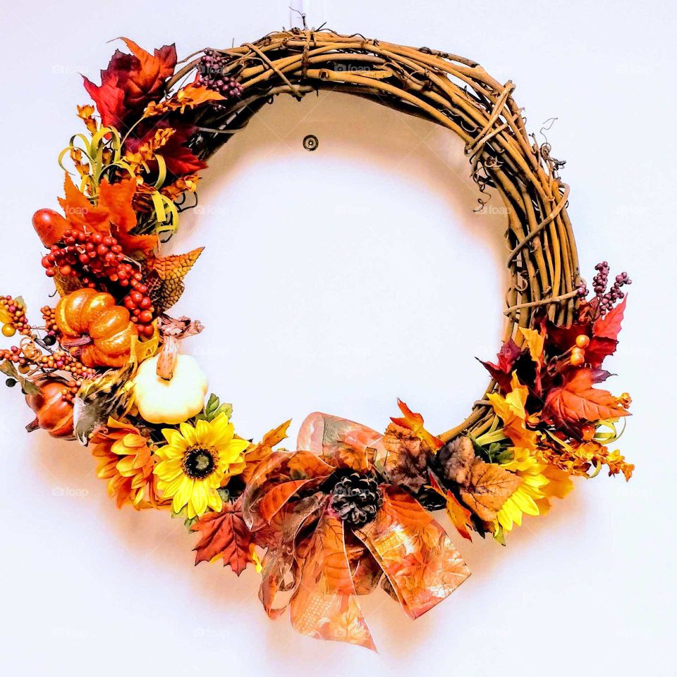 a grapevine Thanksgiving wreath with orange and yellow decorations against a  bright white door