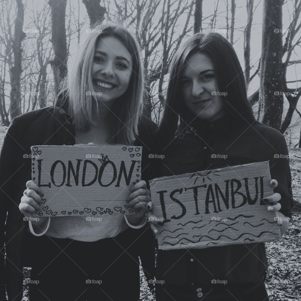Two female friends holding cardboard of London and Istanbul text