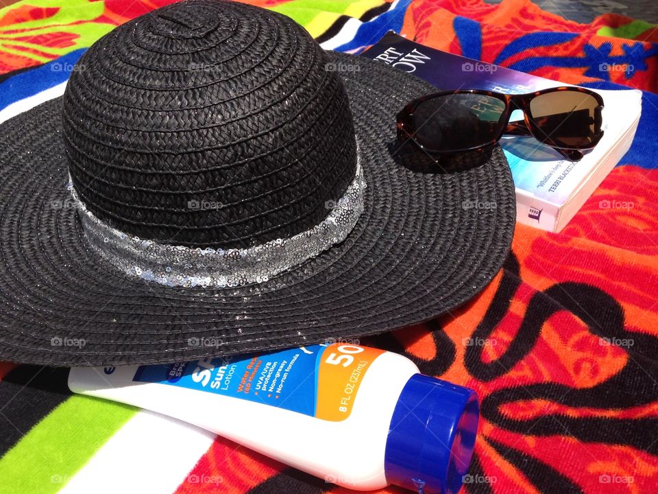 Beach time. Beach hat on beach towel with sunscreen, book, and sunglasses