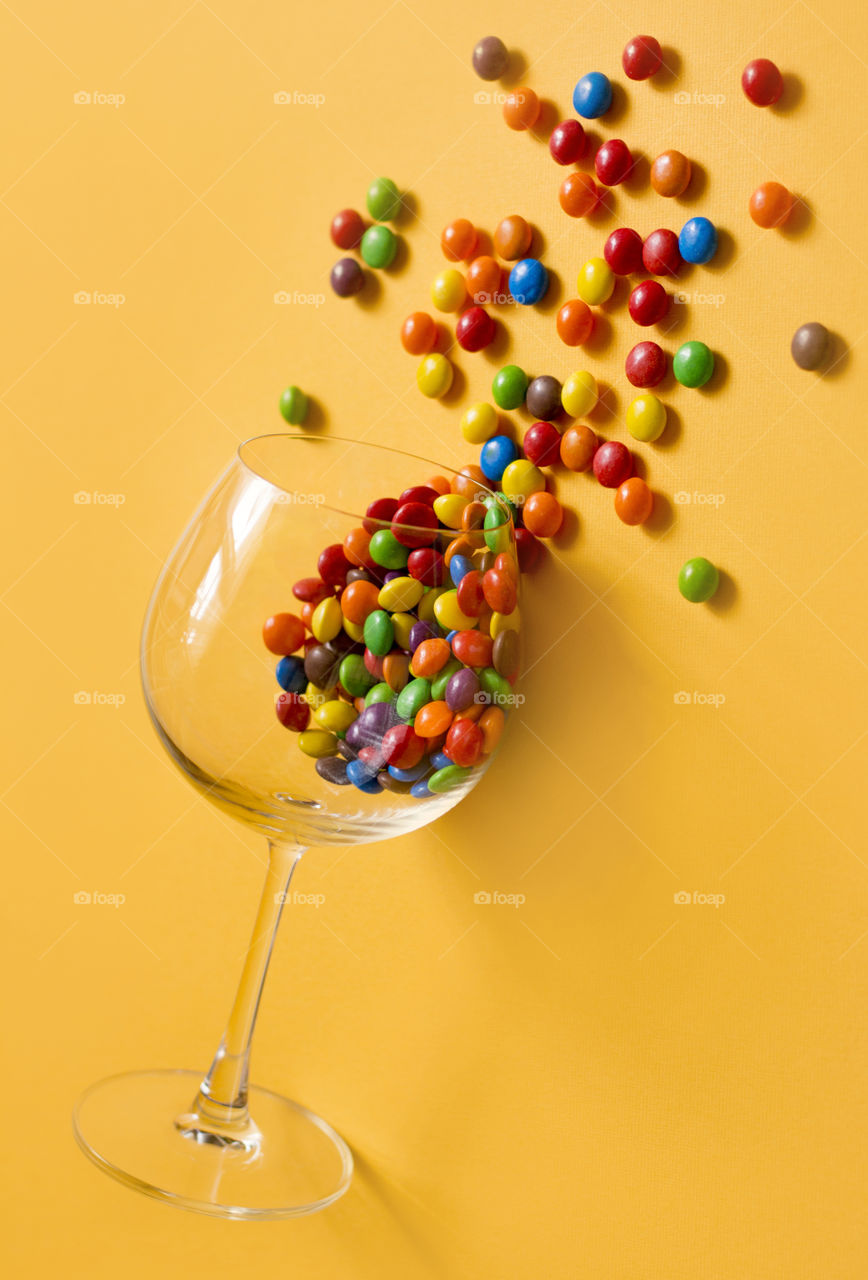 Party time with M&M's candies. Sweets in wine glass on yellow background