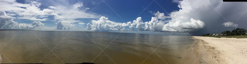 A dark sky infringes on a blue and white cloudy sky above the brown brackish water of the United States side of the Gulf Of Mexico.