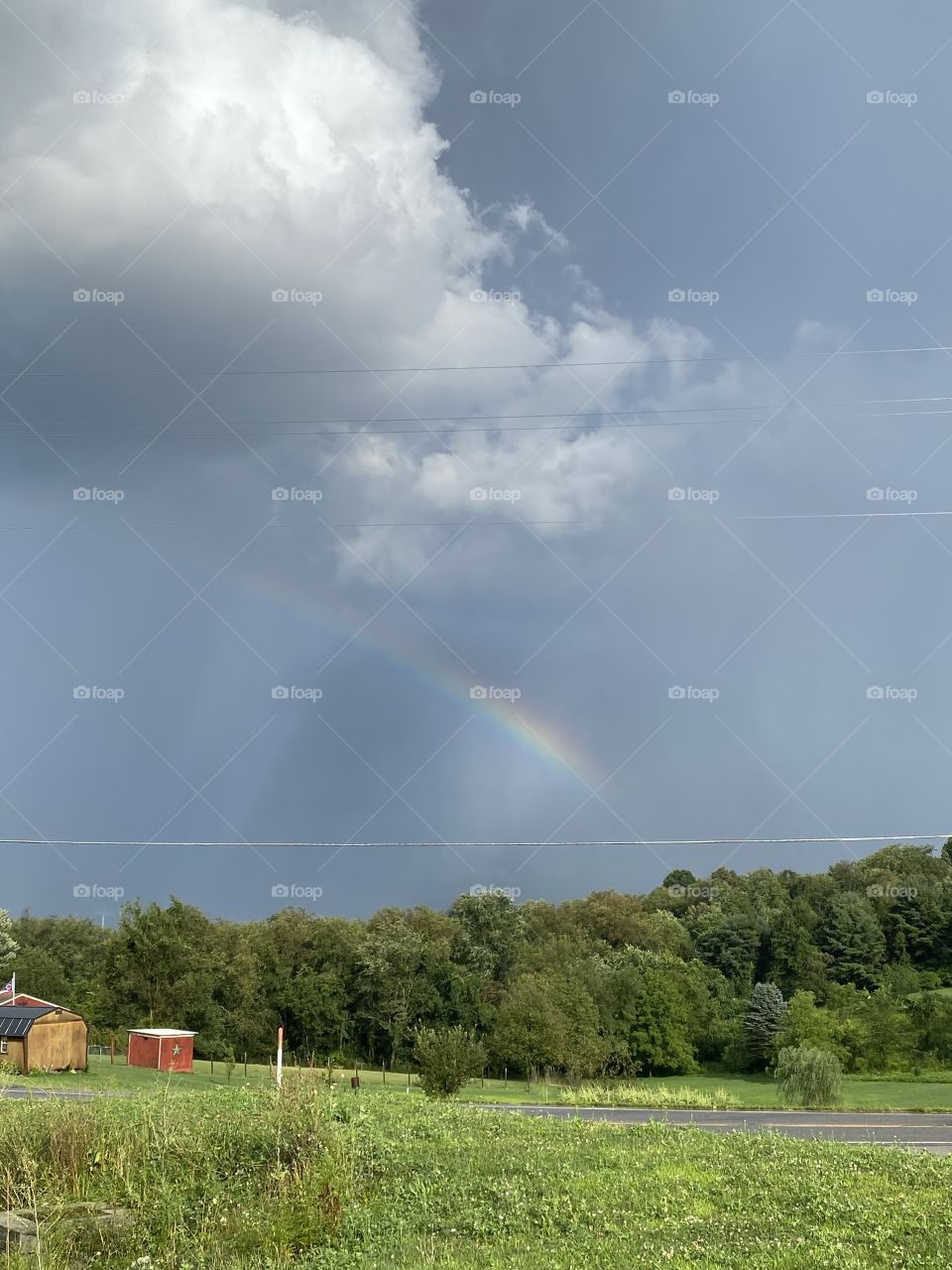 Rainbow in the sky above a field of green and a house with a little storage shed