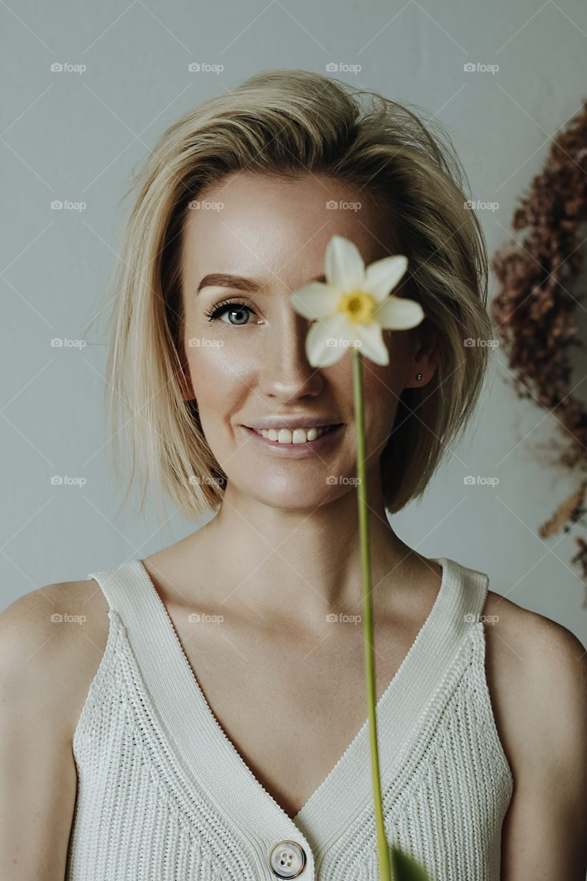 Portrait of a beautiful blonde girl who is holding a narcissus flower which close on of her eyes