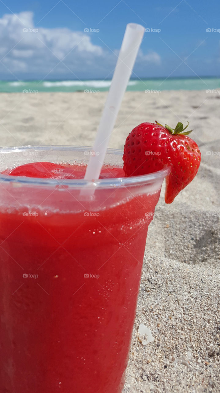 Red drink with strawberry - on sandy beach