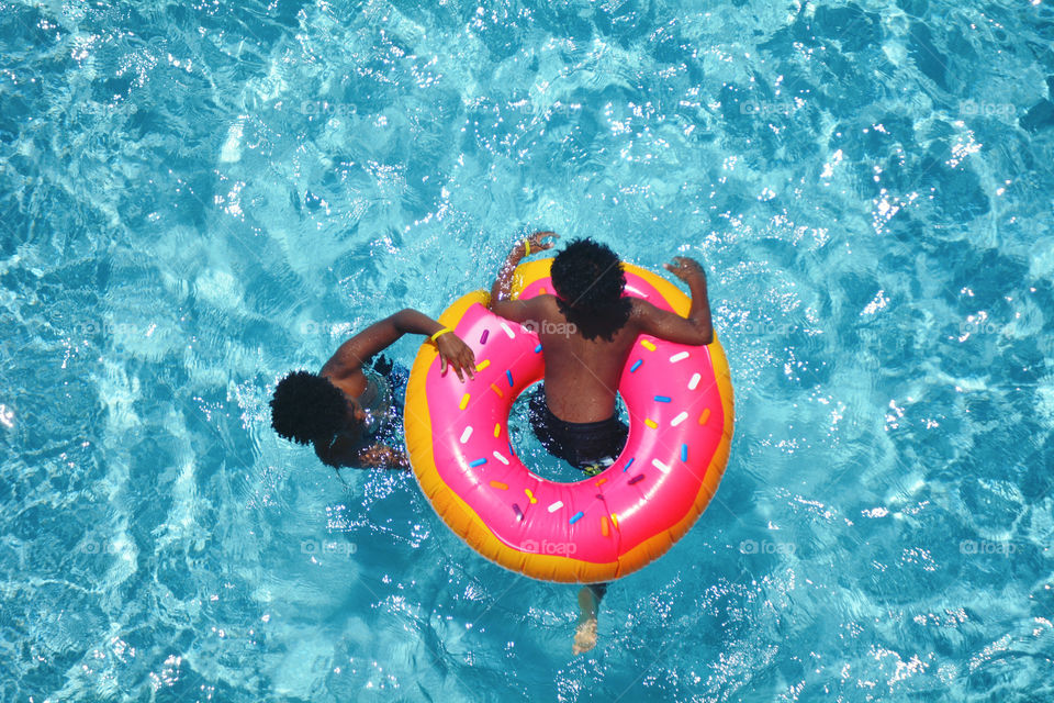 Two boys playing with a donut shaped pool ring in a swimming pool. 
