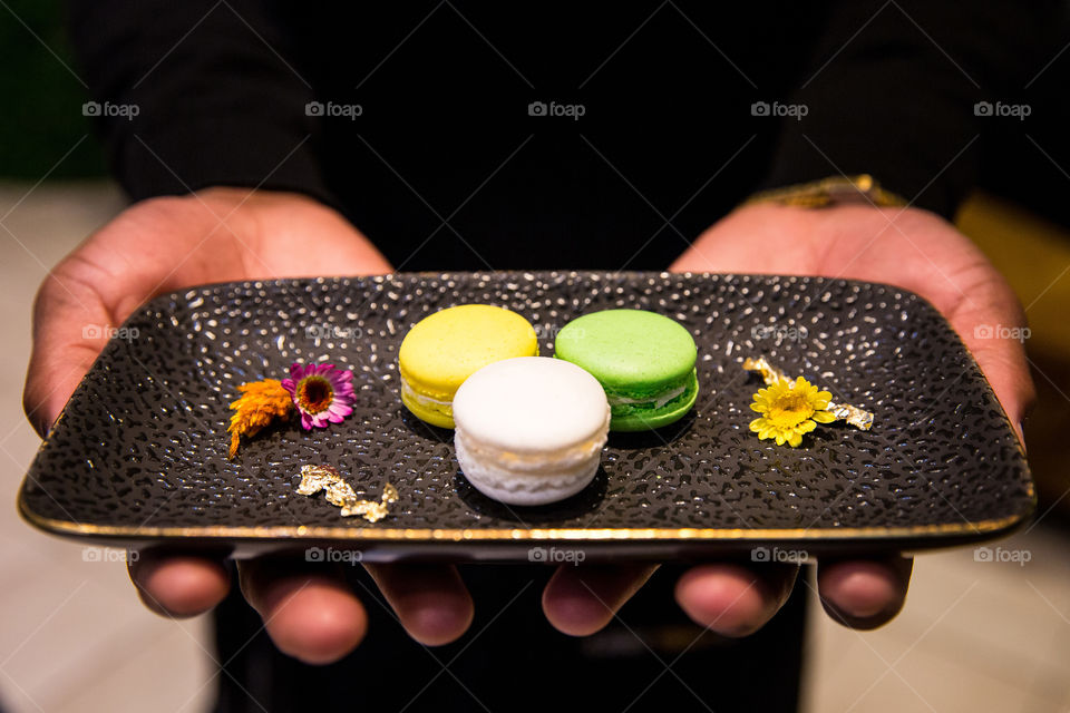 Sweet and sugar! Delicious macaroons on a black plate served by African person.