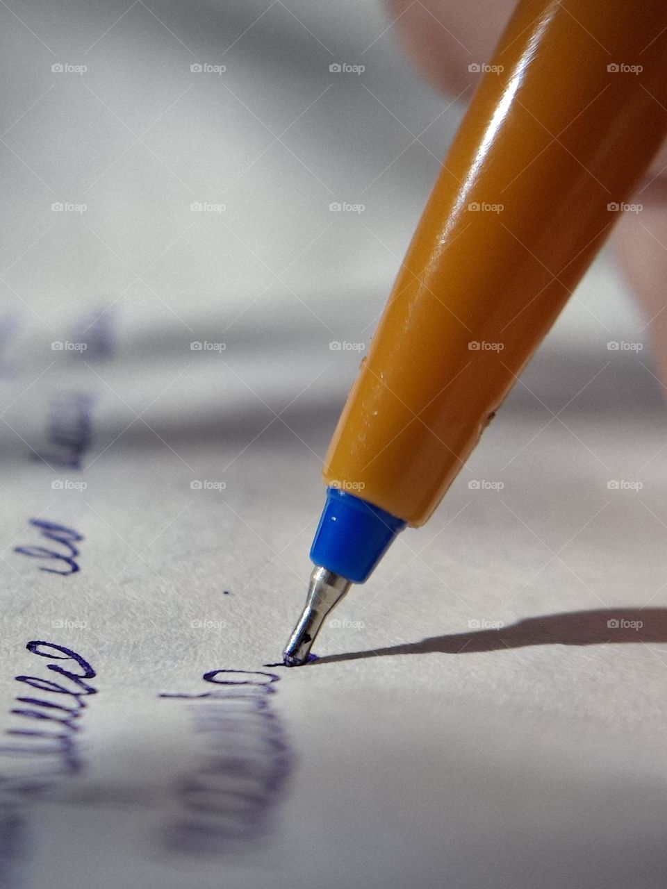 Macro shot of a ballpoint pen writing with blue ink on white paper, highlighting the strong complementary contrast between the orange pen and the blue ink
