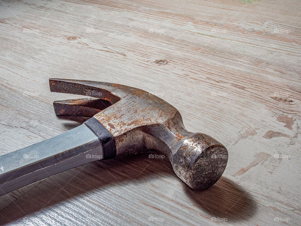 An old rusty iron construction hammer gray with blue color lies on a wooden light background.