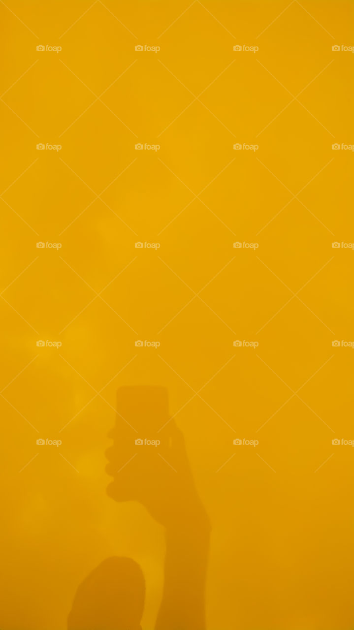 The shadow of the mobile phone holding the boy in the yellow background