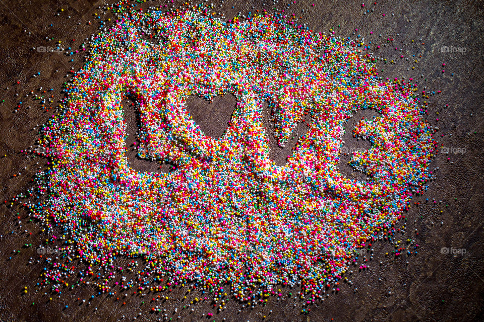 Word love written in multi colored cake and ice cream sprinkles. Love the bright colors! Heart shape love on a dark textured background.