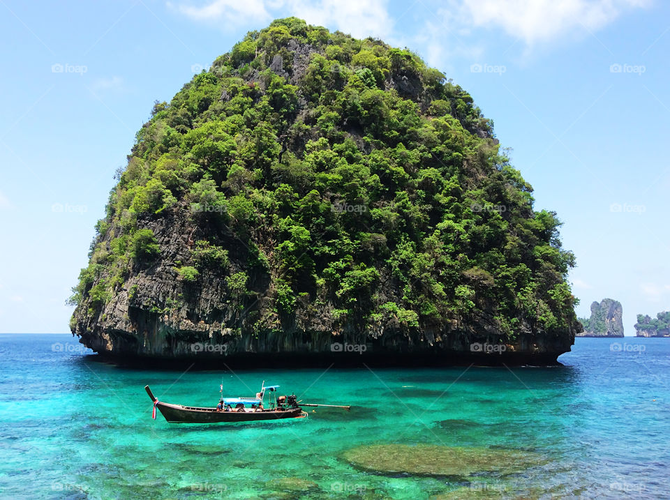 A boat in front of green tropical island in Thailand in the clear turquoise sea water 