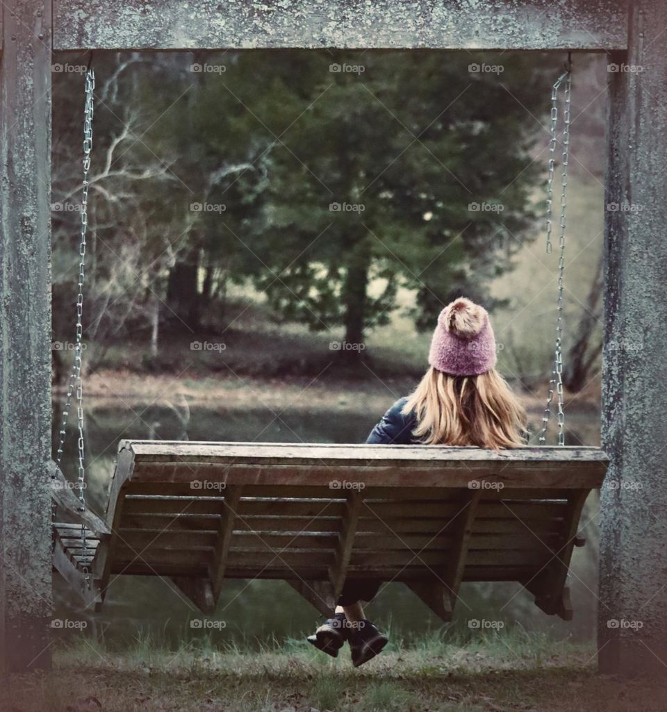 A woman takes a quiet break on an outdoor swing near a pond during the crisp days of Autumn 