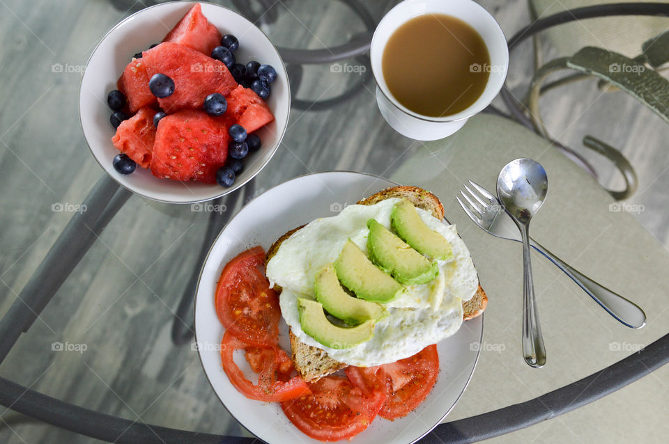 Healthy breakfast of whole grain toast, egg whites, avocado, tomato, watermelon, blueberries, and coffee