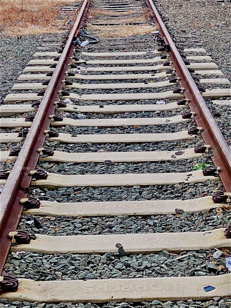Train tracks lead into the distance by the parking lot beneath the Pulaski Bridge in LIC, Queens. Pebbles of different sizes are strewn in between and the various shades of grey combine to an interesting composition. 2021. Hypnotic Productions