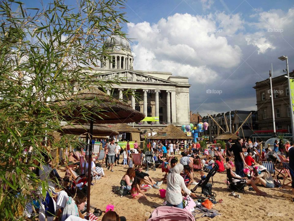 People enjoying good weather on the artificial beach in the Old Market Square with the Council House in the background, Nottingham, England, UK