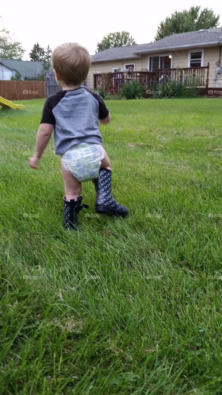 country boy. child walking the backyard in oversized rain boots