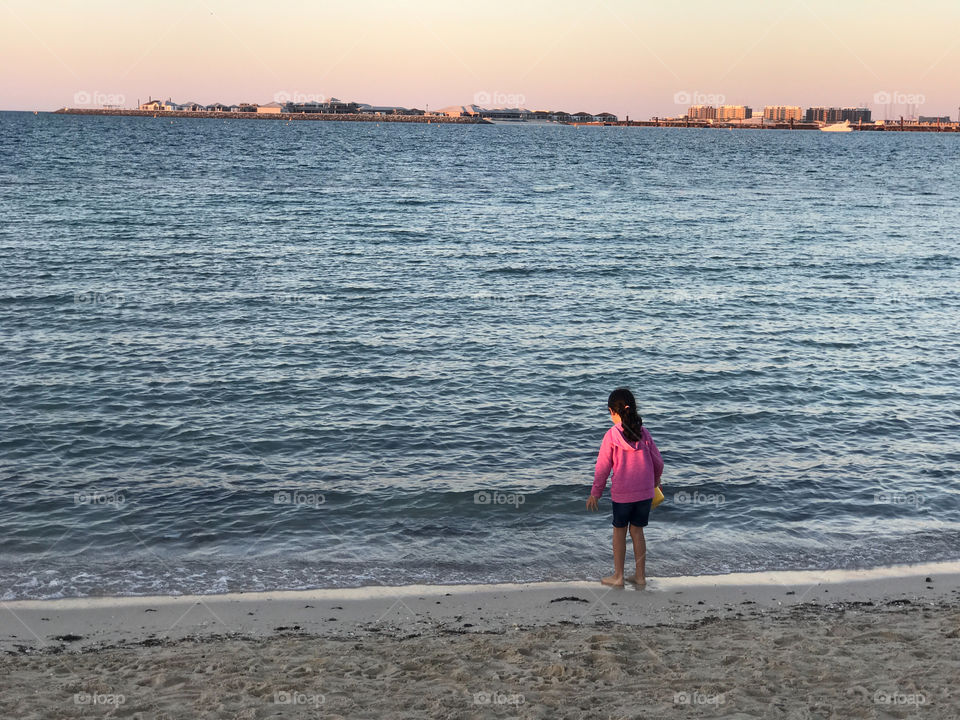 Small girl alone on the beach looking at the sea during sunset