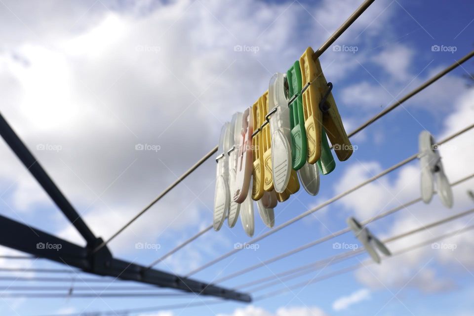 Cloth clips or pegs hanging on a clothes line outdoors under a blue sky with white clouds