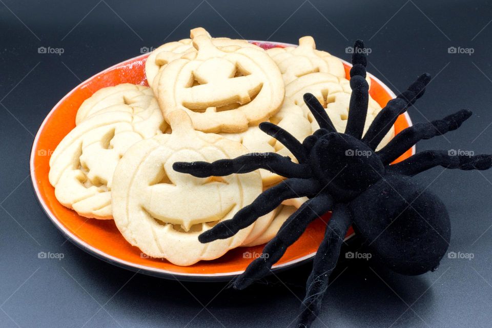 Halloween pumpkin-shaped cookies with a toy spider.