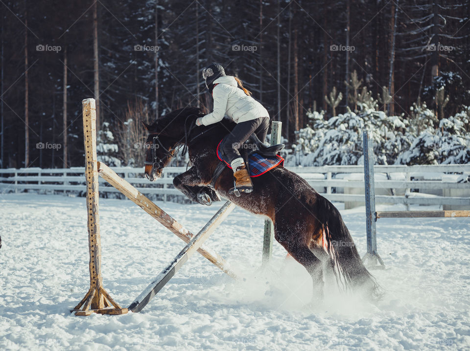 Teenage girl horseback jumping at cold winter day 