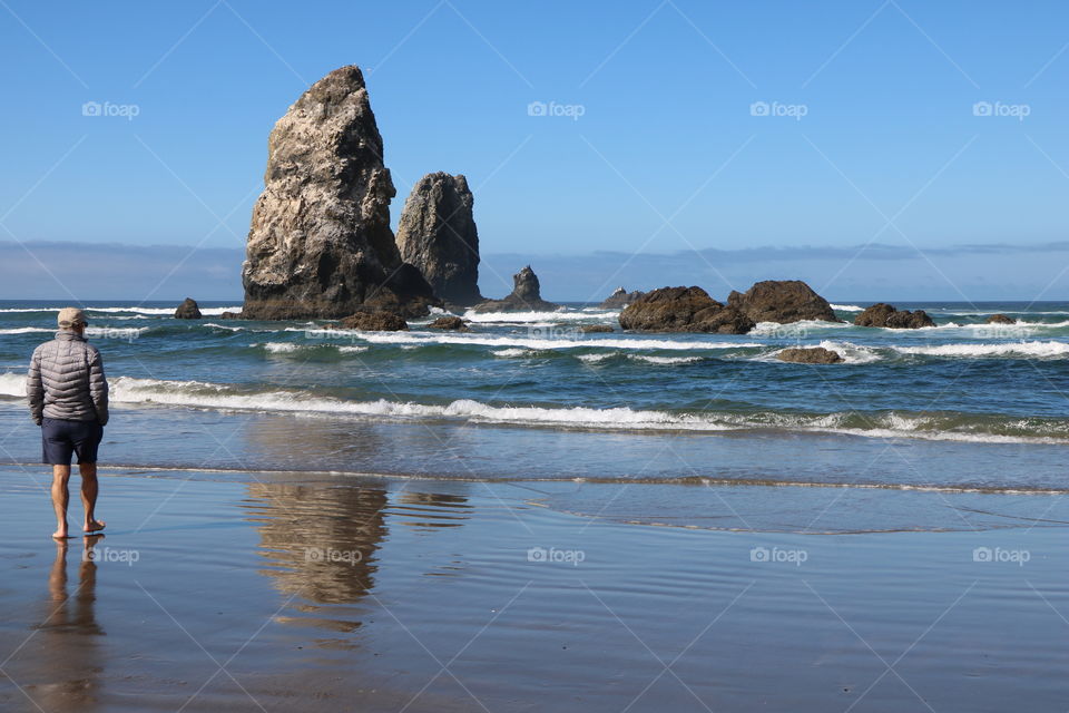 Man on the beach walking towards the big rocky creations reflecting into the blue ocean